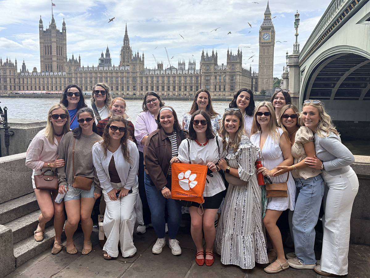 Group of women posing by the River Thames with the Houses of Parliament, Big Ben, and Westminster Bridge in the background, holding an orange flag with a paw print.