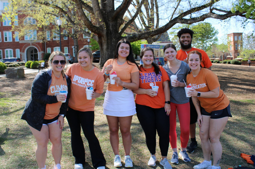 Group of students in orange Clemson shirts smile while enjoying snowcones on Bowman Field.
