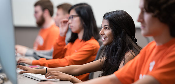 Female student smiles while working on her computer with other students on her left and right.