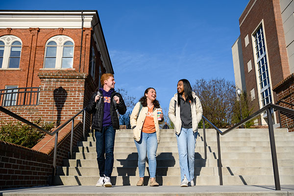 Three students laugh with eachother while walking on campus