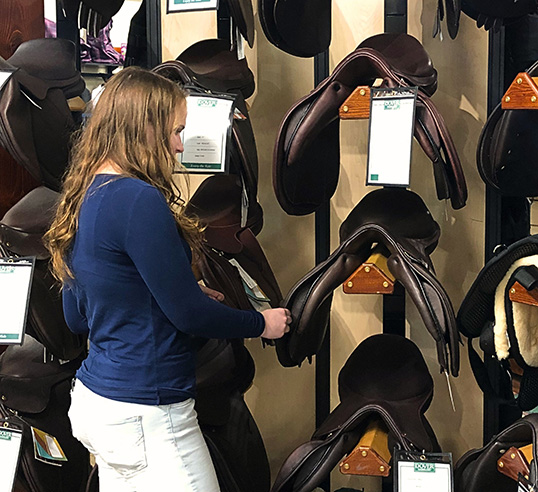 girl standing in front of wall of saddles