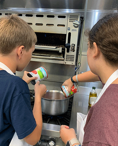 Two kids making pasta sauce
