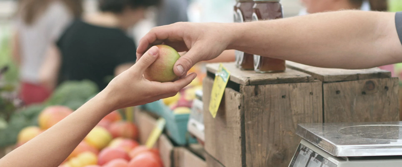 an adult arm passing an apple to a younger person's extended arm