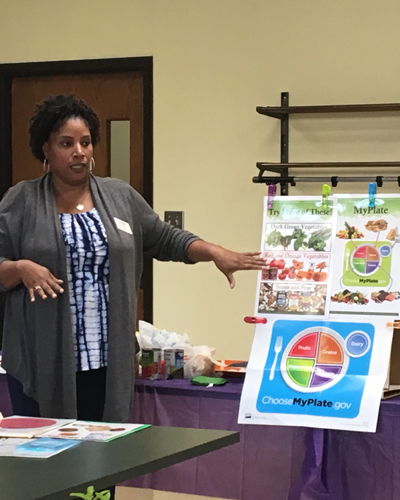 Woman stands beside MyPlate poster with arm extended towards poster