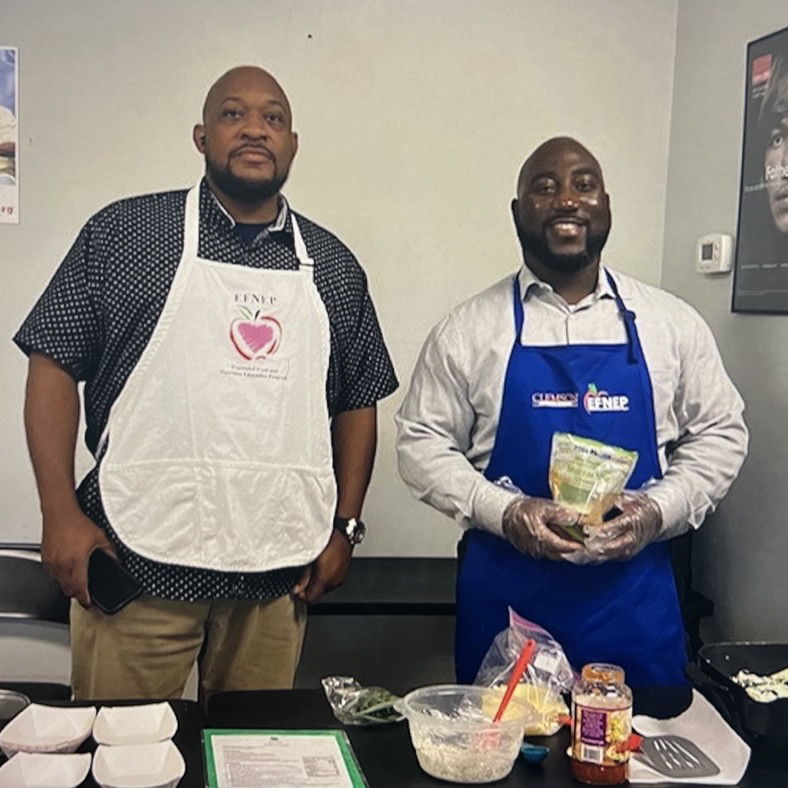 2 men standing behind a food prep table