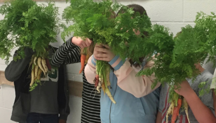 Children holding up produce grown from the School Gardening program.