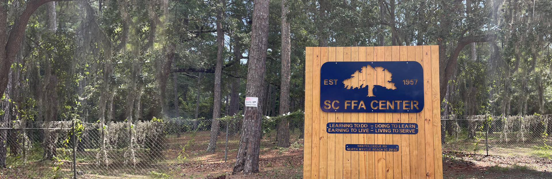 group of ffa members swooden sign in a wooded area at the entrance of the south carolina ffa leadership center  on a bridge smiling