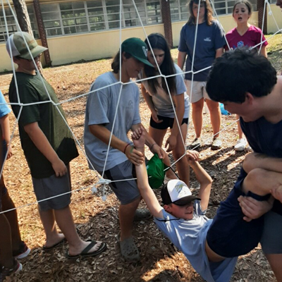 group of students maneuvering through an obstacle in a low ropes team challenge course