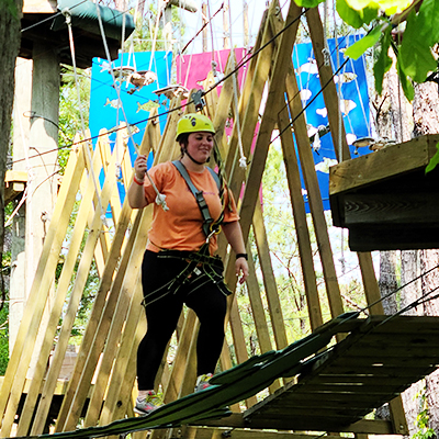 female walking on a platform between trees on a high ropes course