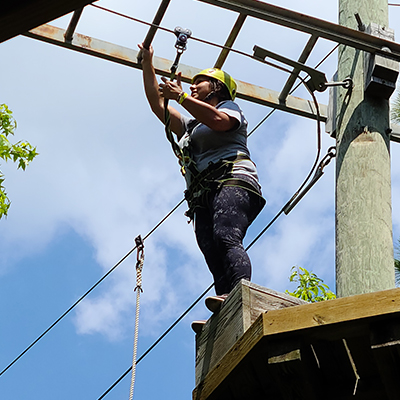 female camper standing on a platform between trees navigating a high ropes course