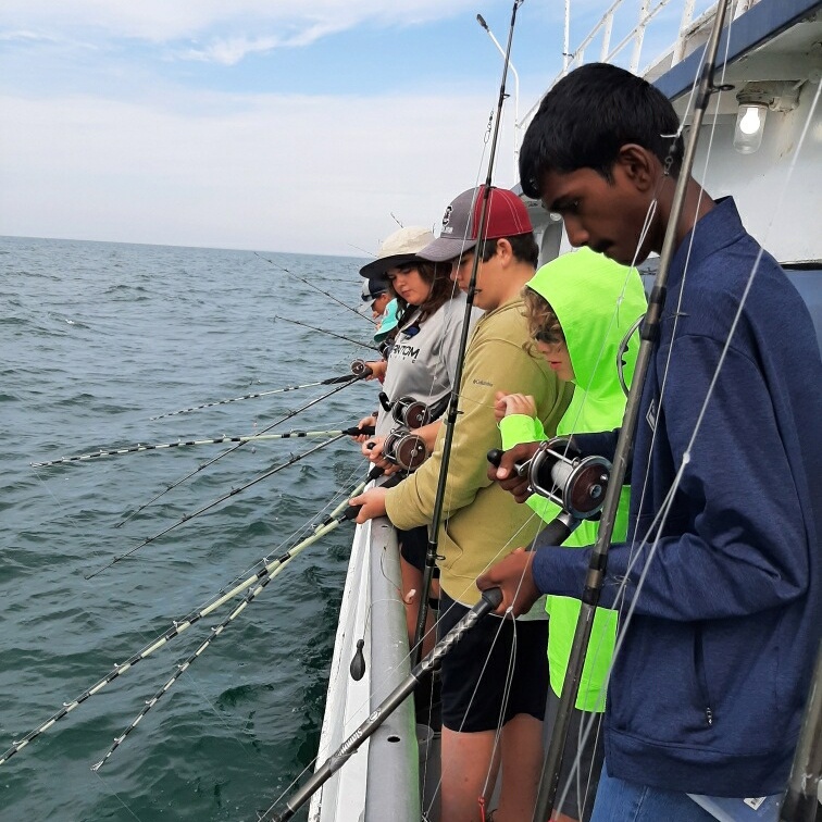 students standing on the side of a boat working with fishing poles