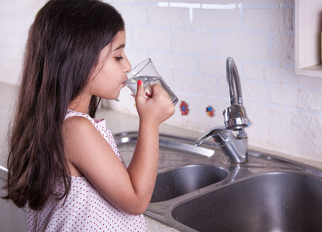 girl drinking water from a glass in front of the sink