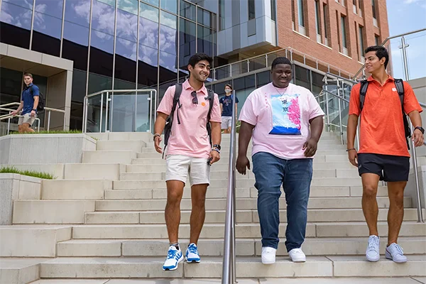 three male students walk down the step of an academic building