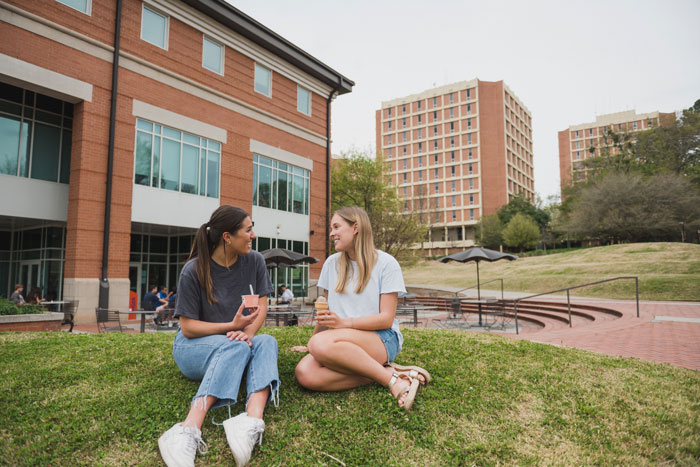 two female students sit on the grass talking outside 55 exchange and the high rises