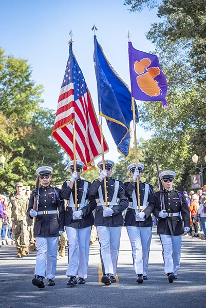 Three Student Marines walk carrying flags in procession