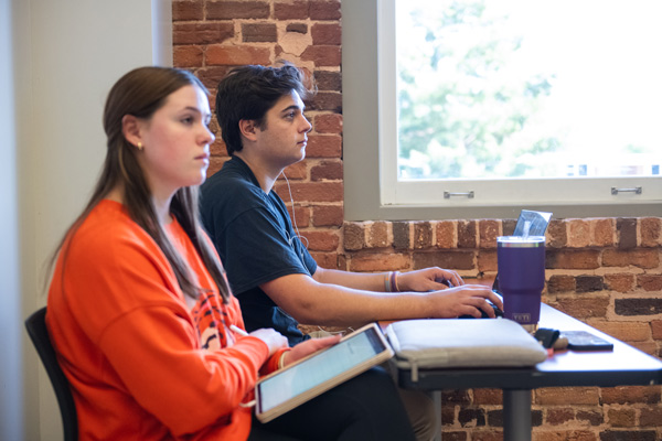 two students sit at their laptops during a lecture