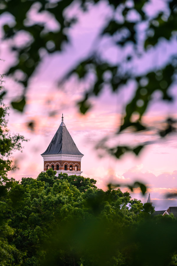 The sun sets behind the old main clock tower coloring the sky orange and purple