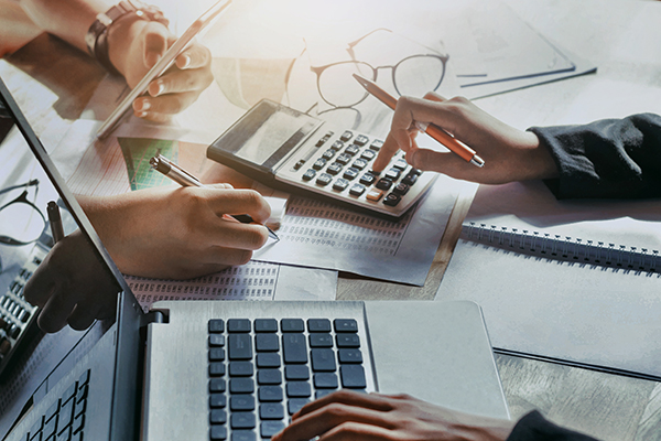 Hands working on financial calculations with a calculator, laptop, and documents on a table.