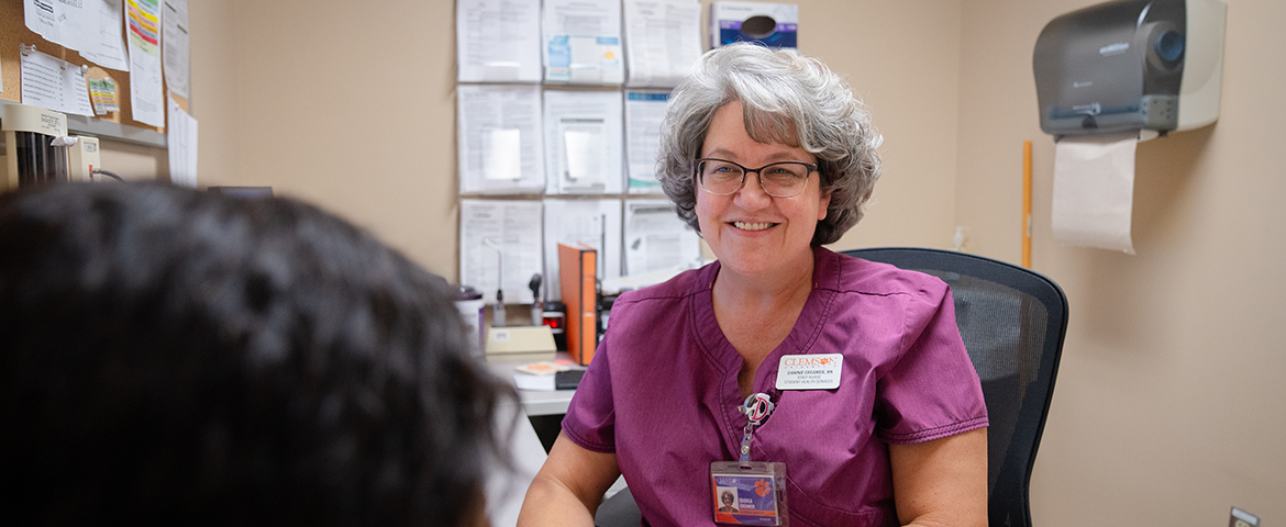Person in nurse's scrubs sitting and smiling as they speak to a person outside of view