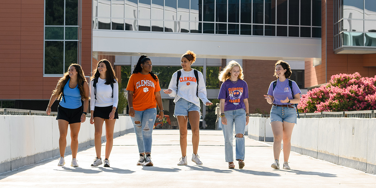 Six Clemson Students walk across a campus bridge chatting happily.
