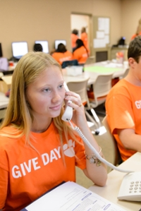 Two people in orange shirts answering phones for the phonathon event