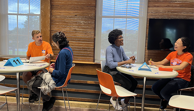 Two pairs of students sit at two tables, chatting and laughing together