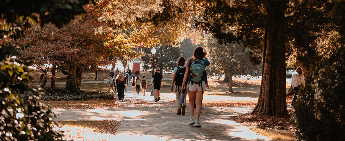 Students walking in autumn surrounded by trees with orange and gold leaves
