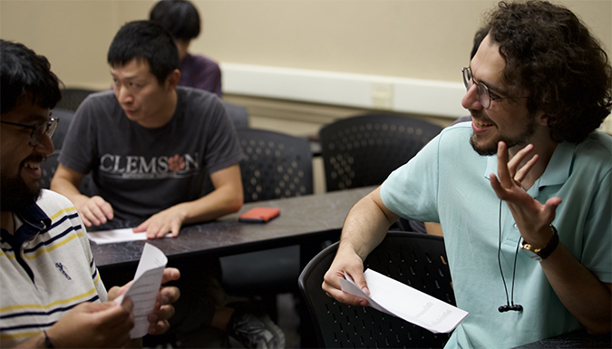 Two students sit together at a table in the library, smiling and chatting