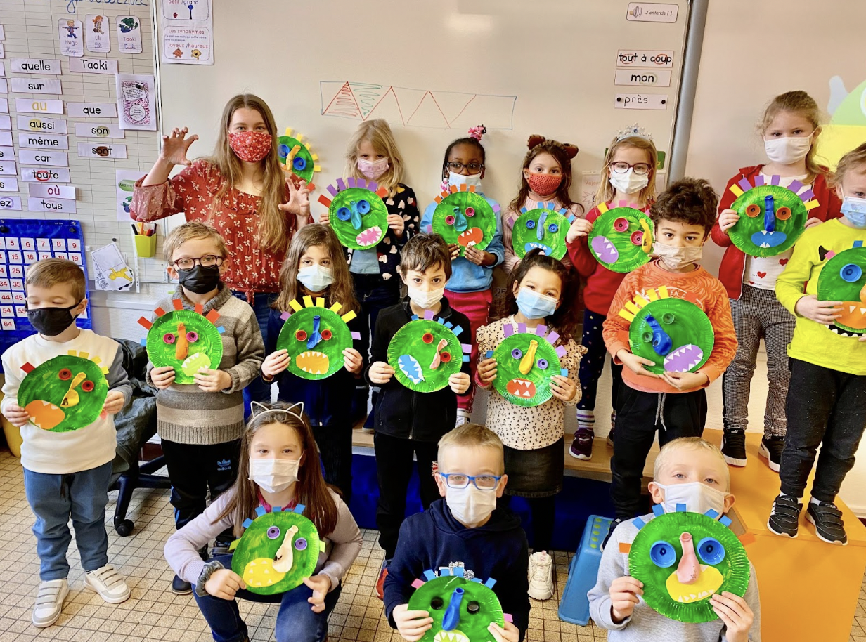 Clemson TEFL student poses with a group of elementary school students displaying their artwork