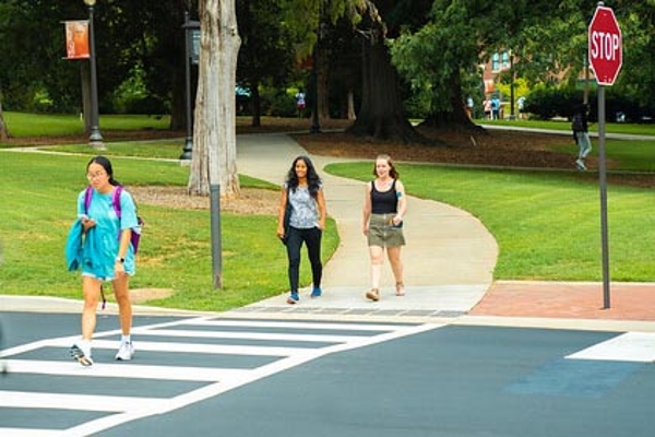 Three students at a crosswalk on campus making conversation