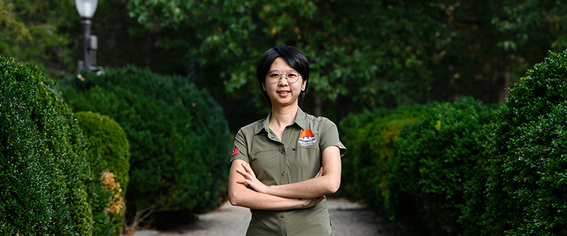 Headshott of Hsuan Hsieh standing and surrounded by bushes and trees in the background