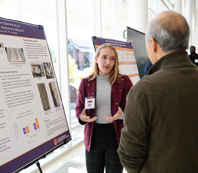 A woman and man in professional attire chat in front of a presentation posterboard