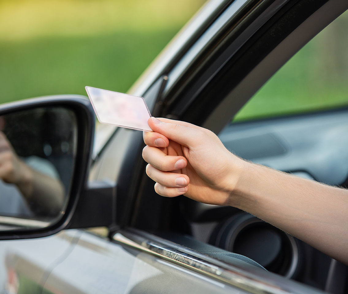 A driver's arm extends out the car window, holding a driver's license