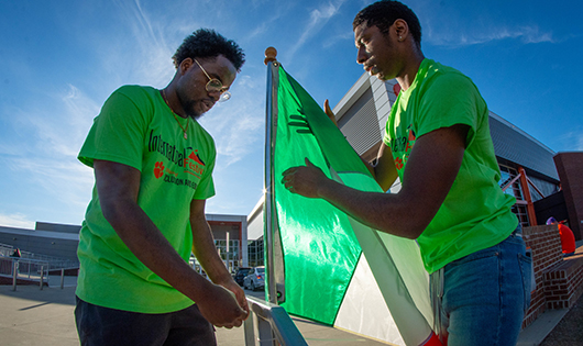 two men put their country's flag on a flag pole at the international festival