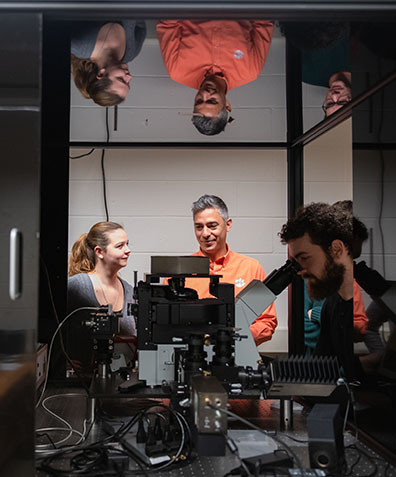 Dr. Sanabria talks to a female graduate student while a male student looks through a microscope