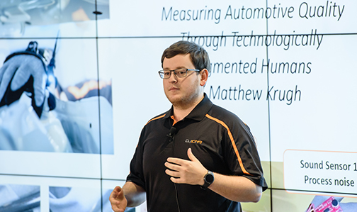 a student presents automotive research in front of a large video screen