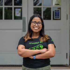 Dr. Pro Manna smiling wearing a black t shirt in front of a brick building