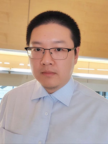 Head-and-shoulders portrait of a person wearing glasses and a light blue button-up shirt indoors.