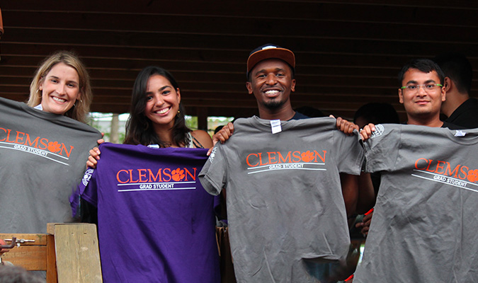 group of four smiling students displaying Clemson grad student t-shirts