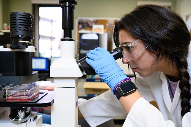 female in a lab looking through microscope