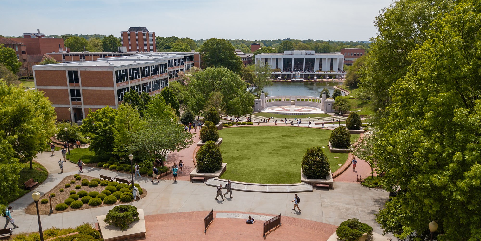 Clemson University students walking to campus with the amphitheater, reflection pond, and library in the background.