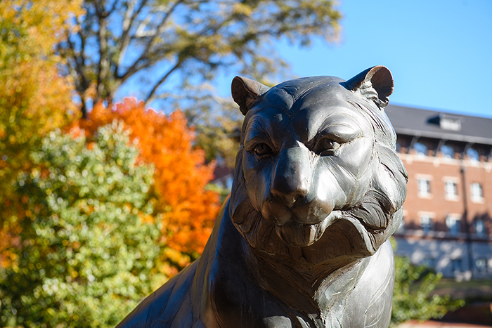 A tiger statue with blue sky and autumn colors in the background.