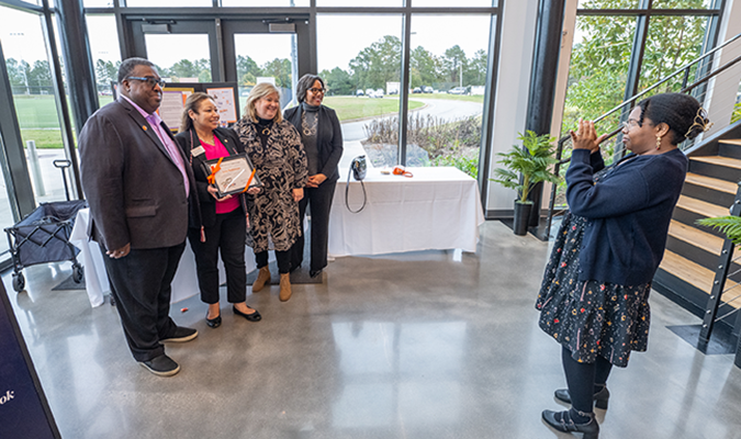 A woman takes a photo of a group of four people. One woman is holding a certificate.