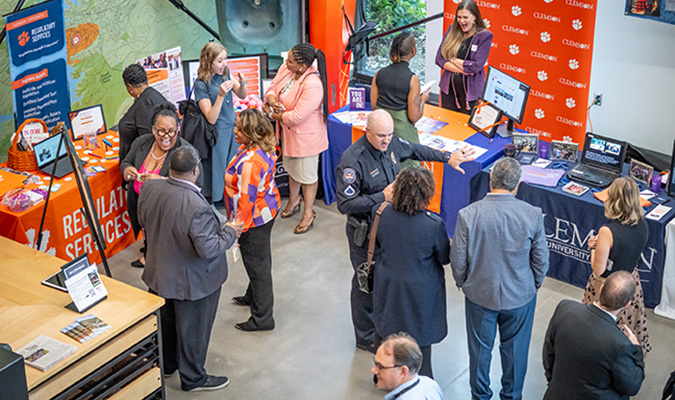 Groups of people have conversations in an atrium. Some individuals are standing in front of tables with displays on them.