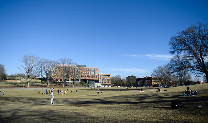 People walk around Bowman Field with the Powers College of Business in the background.