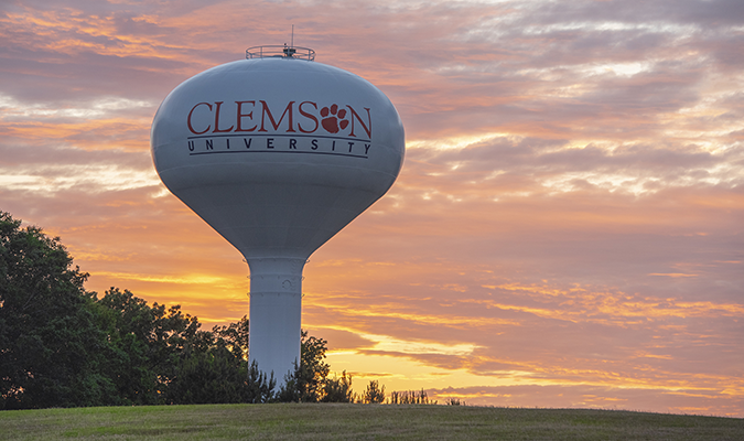 The setting sun illuminating the sky behind a Clemson University water tower.