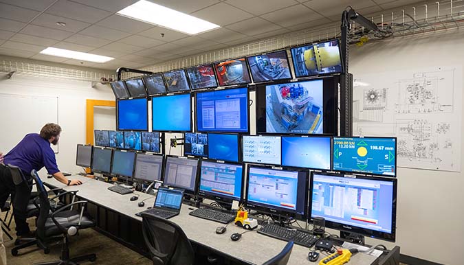 Staff member reaches over to use a keyboard connected to a station of computers with several monitors.