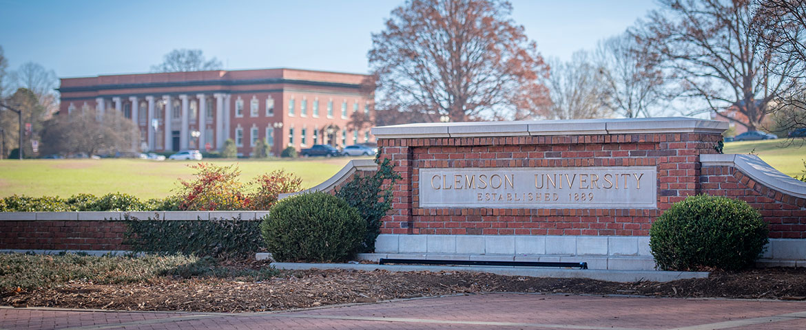 Brick Clemson University sign in the foreground with a slightly out of focus Sikes hall in the background.