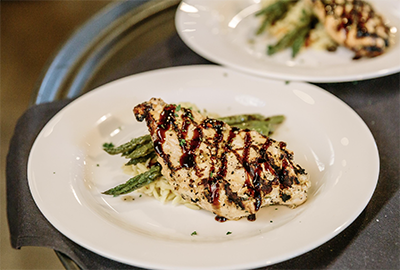 Grilled chicken breast drizzled with balsamic glaze, served over a bed of asparagus and pasta.