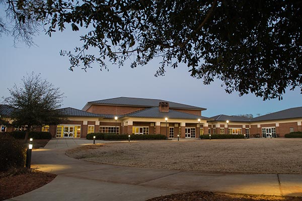 A well-lit building surrounded by landscaped grounds during twilight.